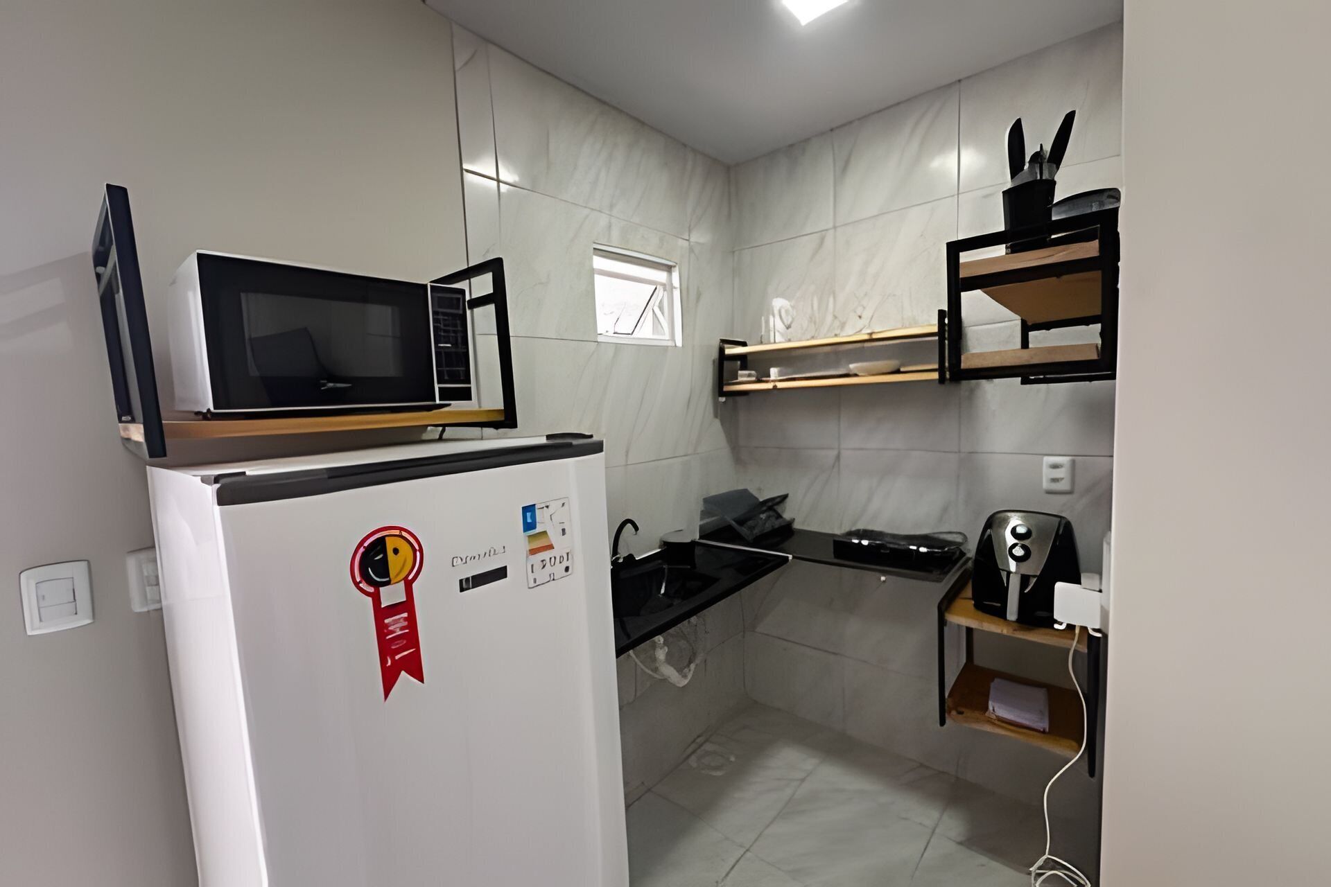 A compact kitchen with a microwave on top of a white refrigerator, a black stove, and a coffee maker on a wooden shelf.