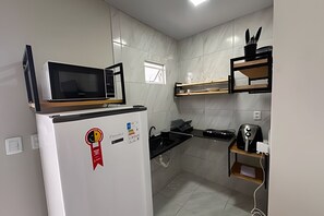 Une cuisine compacte avec un four à micro-ondes posé sur le dessus d’un réfrigérateur blanc, une cuisinière noire et une machine à café sur une étagère en bois.