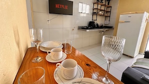 A dining area with a wooden table set for four, a television mounted on the wall, and a kitchen area with a refrigerator and countertop appliances. - AirBNBusiness Maracanaú (Maracanau)
