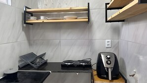 A kitchen with a black countertop, a coffee maker, a hairdryer, and a shelf with cups and plates.