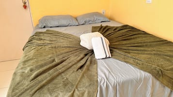 Uma cama com um cobertor e almofadas verdes, uma porta com fechadura e uma tomada.