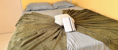 A bed with a green blanket and pillows, a door with a lock, and a wall socket.