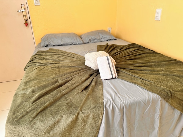A bed with a green blanket and pillows, a door with a lock, and a wall socket. - AirBNBusiness Maracanaú (Maracanau)