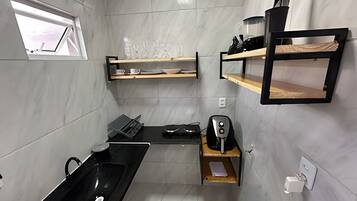 Uma cozinha compacta com uma pia preta, uma máquina de café e prateleiras com utensílios de cozinha.