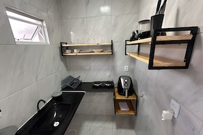 A compact kitchen with a black sink, a coffee machine, and shelves with kitchenware. - AirBNBusiness Maracanaú (Maracanau)