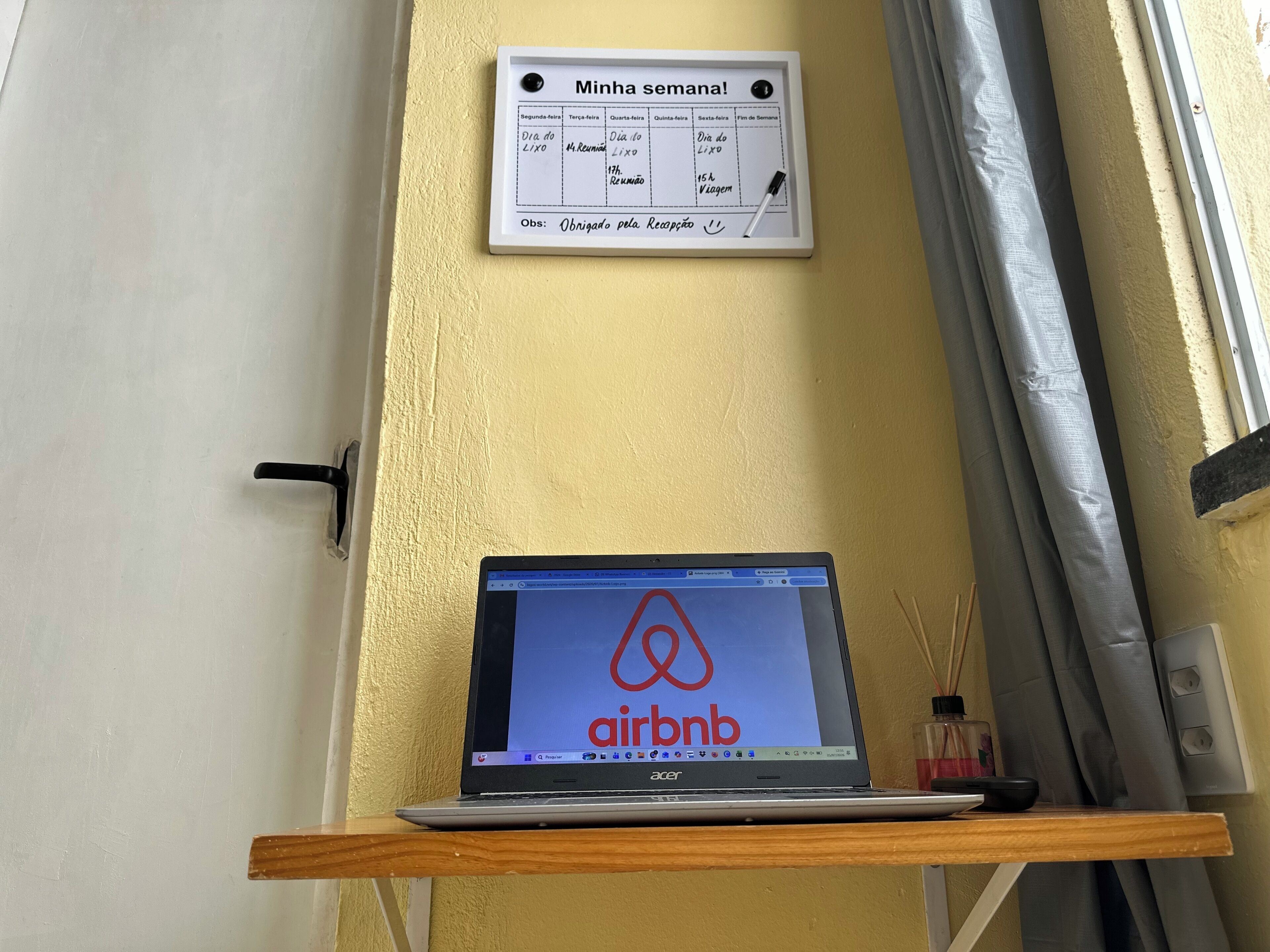 En bærbar computer på en træhylde med Airbnb-logoet, en kalender på væggen og en dør med dørhåndtag.