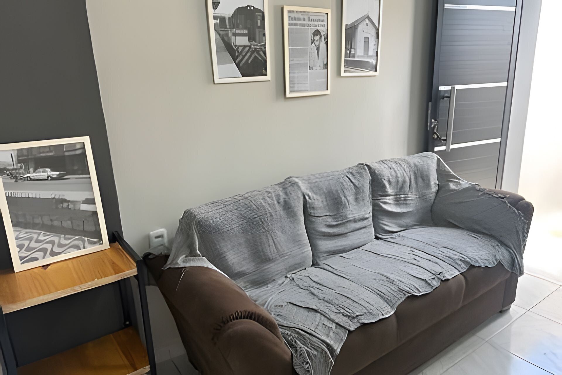 Uma sala de estar com um sofá marrom, uma fotografia emoldurada sobre uma mesa de madeira e três quadros na parede.