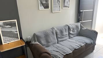 Uma sala de estar com um sofá marrom, uma fotografia emoldurada sobre uma mesa de madeira e três quadros na parede.