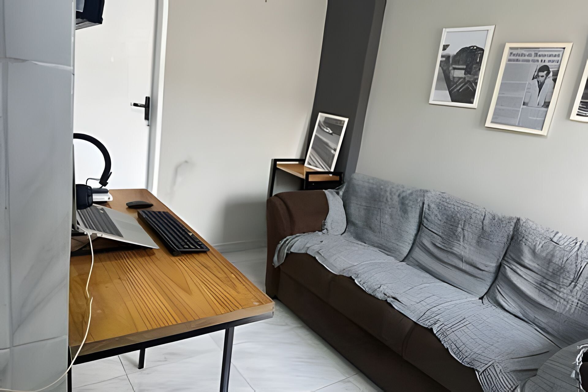 Una habitación con escritorio, computadora, teclado, ratón, silla y sofá. En la pared, hay cuadros enmarcados.