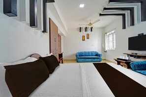 A hotel room with a bed, a blue sofa, a TV, and a ceiling fan. - Classic G K Building (Thindukkal)