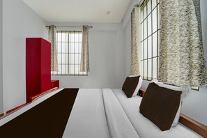 Ein Hotelzimmer mit einem Bett, einem roten Schrank und einem Fenster mit gemusterten Vorhängen.