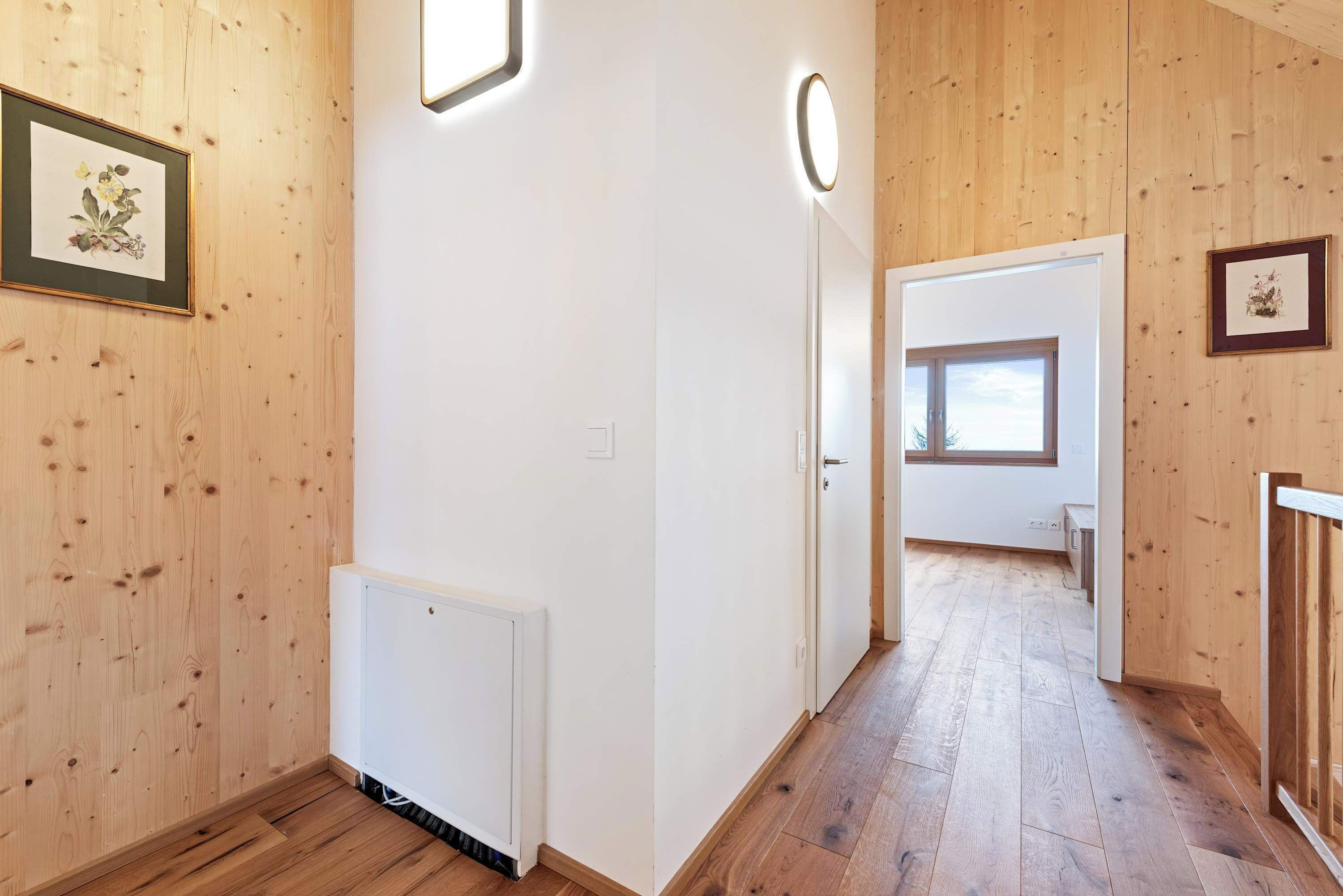A hallway with wooden walls and floors, a white radiator, and framed artwork on the walls.