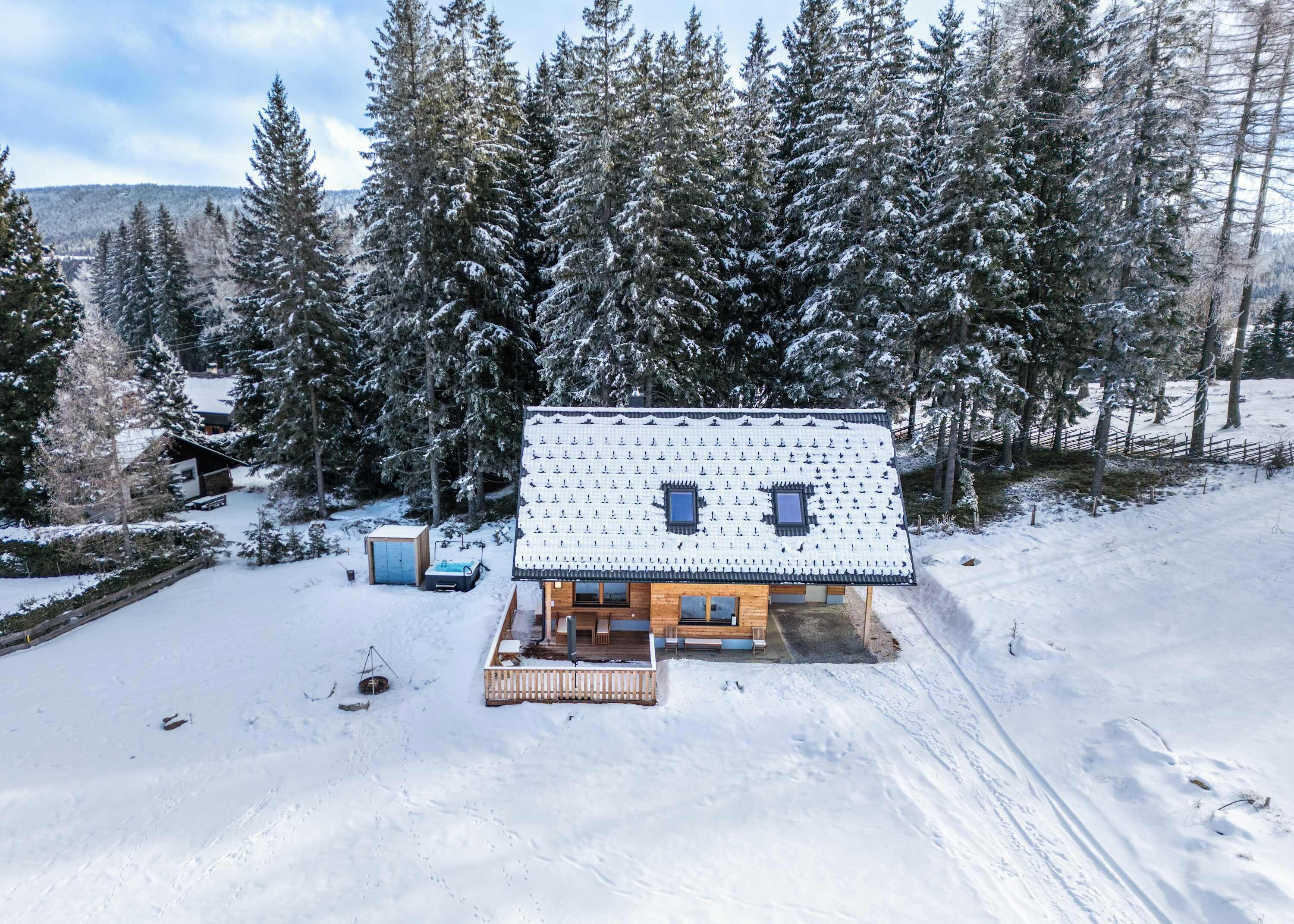 A cabin with a snow-covered roof, surrounded by tall evergreen trees.