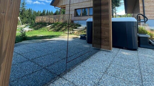 Una cabaña moderna de madera con un patio de piedra, una terraza de madera y vistas a una zona boscosa.