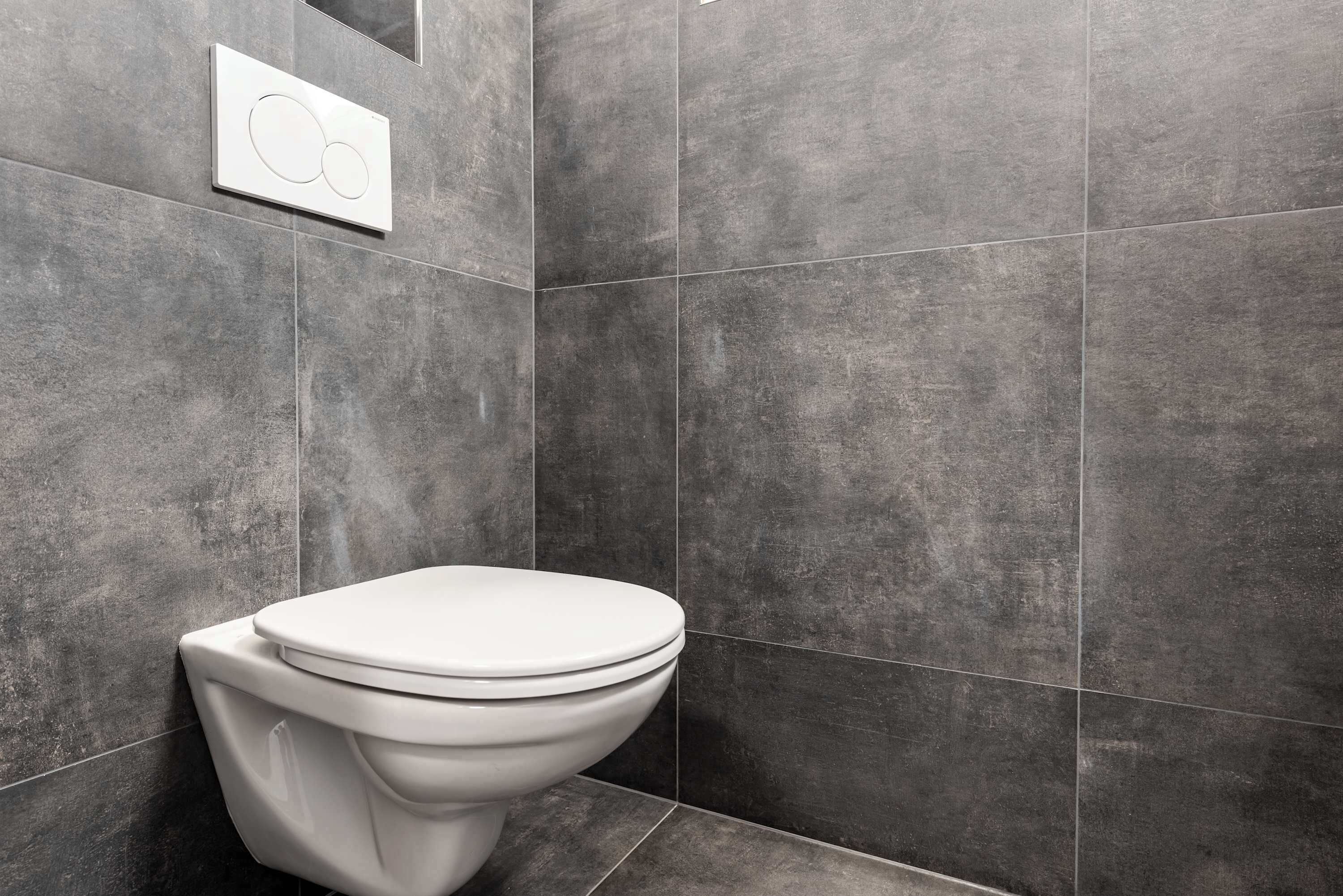Een moderne badkamer met een wit toilet, donkergrijze tegels en een bedieningspaneel aan de muur.