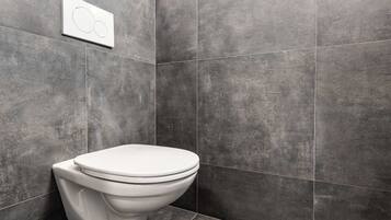 Een moderne badkamer met een wit toilet, donkergrijze tegels en een bedieningspaneel aan de muur.