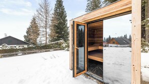 Una cabaña de madera con la puerta abierta, rodeada de nieve en el suelo y árboles.