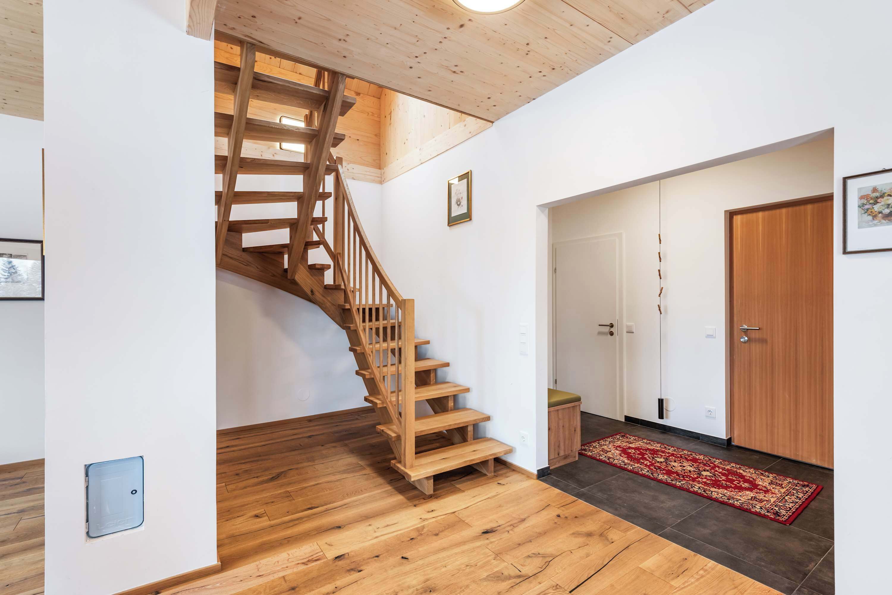 Una escalera de madera que conduce a un segundo piso, una puerta blanca y una alfombra roja en el suelo.