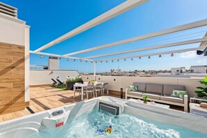 Una terraza en la azotea con jacuzzi, mobiliario exterior y vistas a la ciudad.