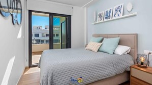 A modern bedroom with a large bed, a nightstand, and a view of the city through a sliding door.