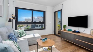 A modern living room with a sofa, a coffee table, a TV, and a large window with a city view.
