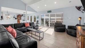 Un vaste espace de vie comprenant un canapé en cuir noir, une table basse et un meuble en bois. Une porte-fenêtre coulissante donne accès à un patio extérieur offrant une vue sur le paysage.