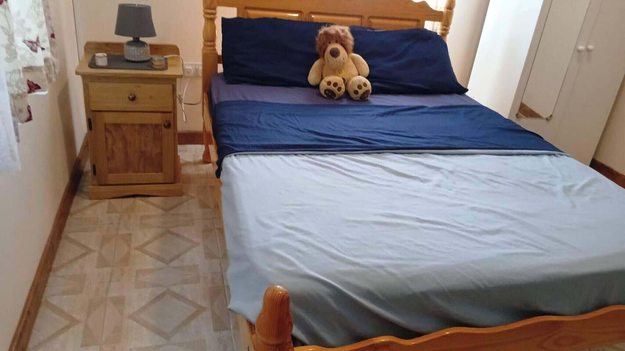 A bedroom with a bed, a nightstand, a teddy bear, and a wardrobe.