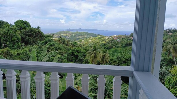 Un balcón con barandilla blanca que da a un paisaje verde exuberante con colinas y una vista distante del mar.