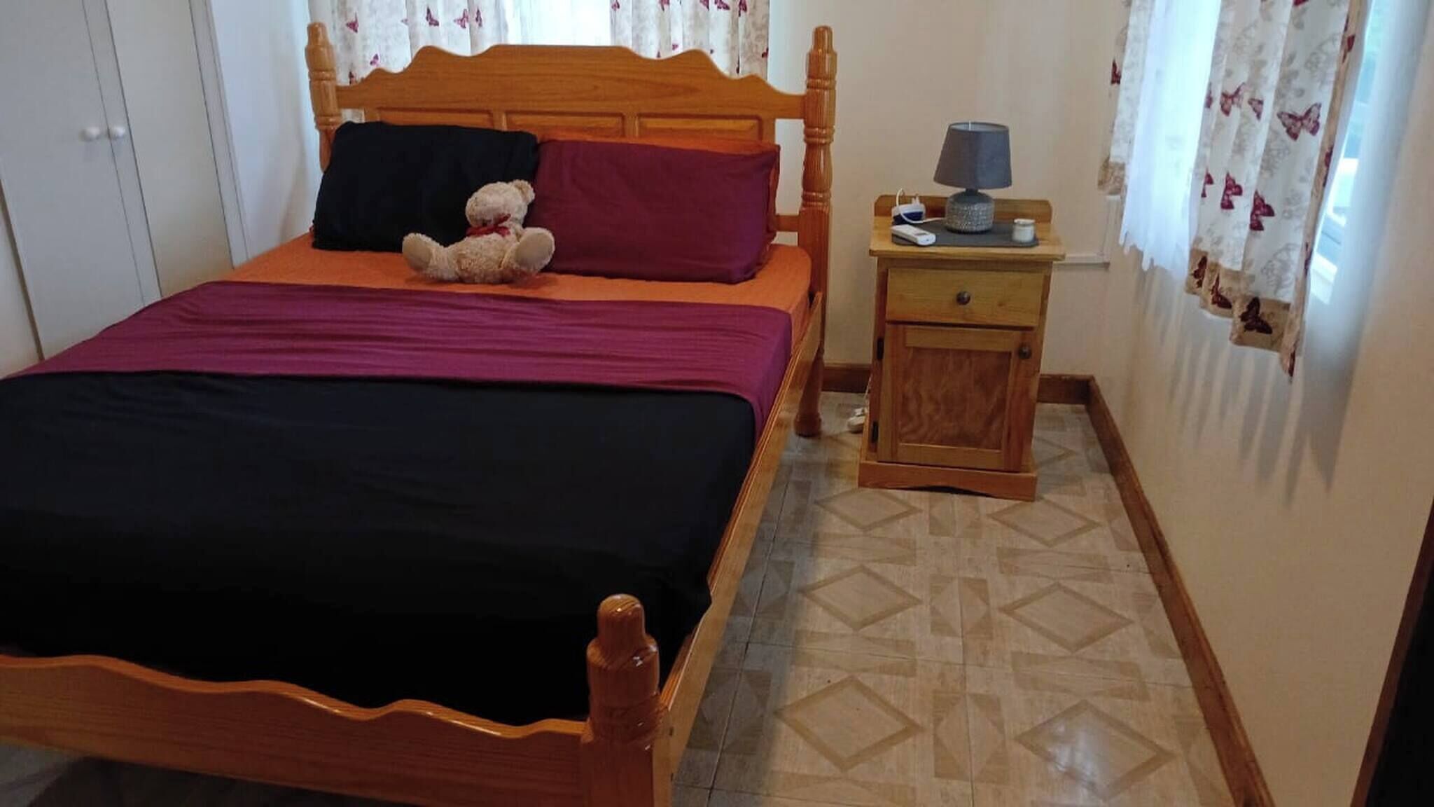 A bedroom with a wooden bed, a nightstand, a lamp, and a teddy bear.