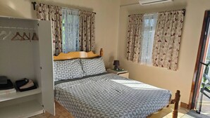 Un dormitorio con cama, armario, mesita de noche y ventana con cortinas.