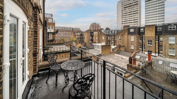 Een balkon met een tafel en stoelen, en uitzicht op de stadsgezicht, met een bakstenen gebouw.