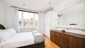 Een moderne slaapkamer met een groot bed, een houten dressoir, een spiegel en een raam met gordijnen.