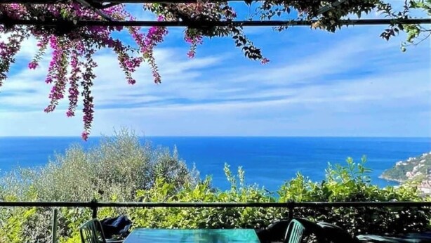 Een terras met een tafel en stoelen, met uitzicht op de kust, zee en een heldere lucht.
