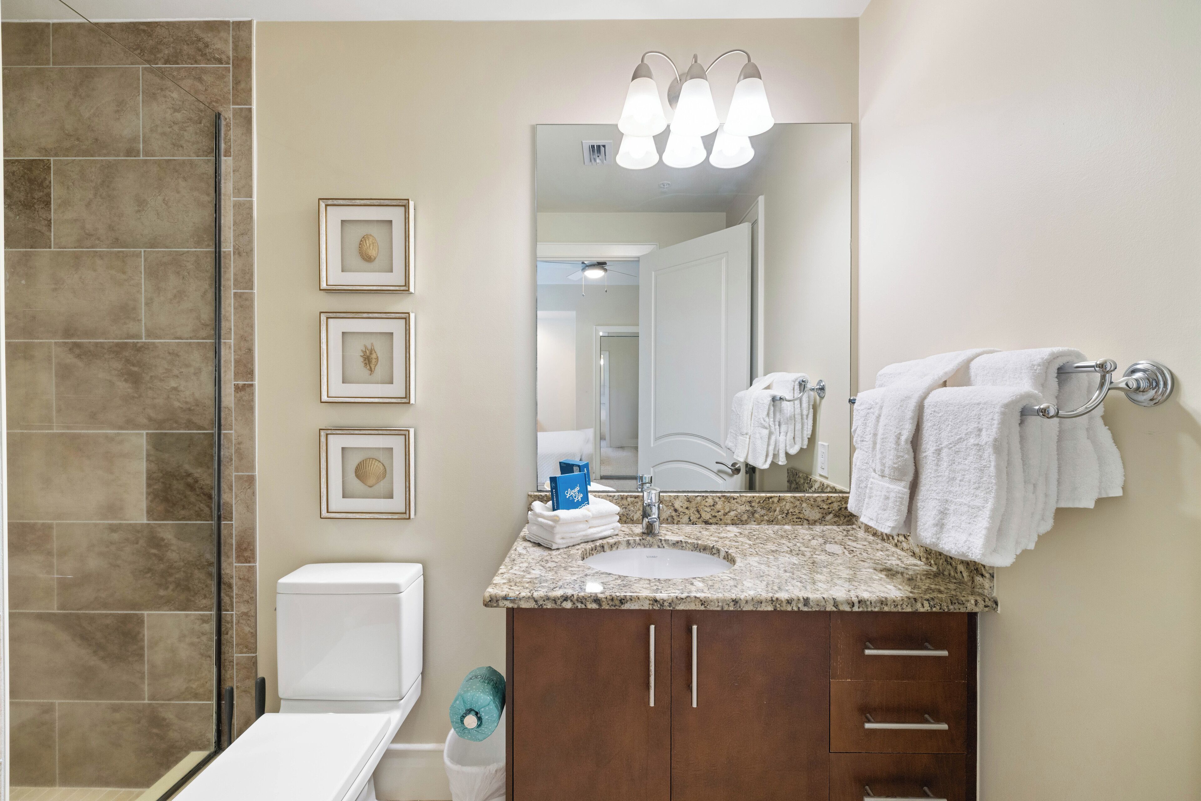 A bathroom with a shower, toilet, sink, and vanity. There are framed pictures on the wall and a towel rack with towels.