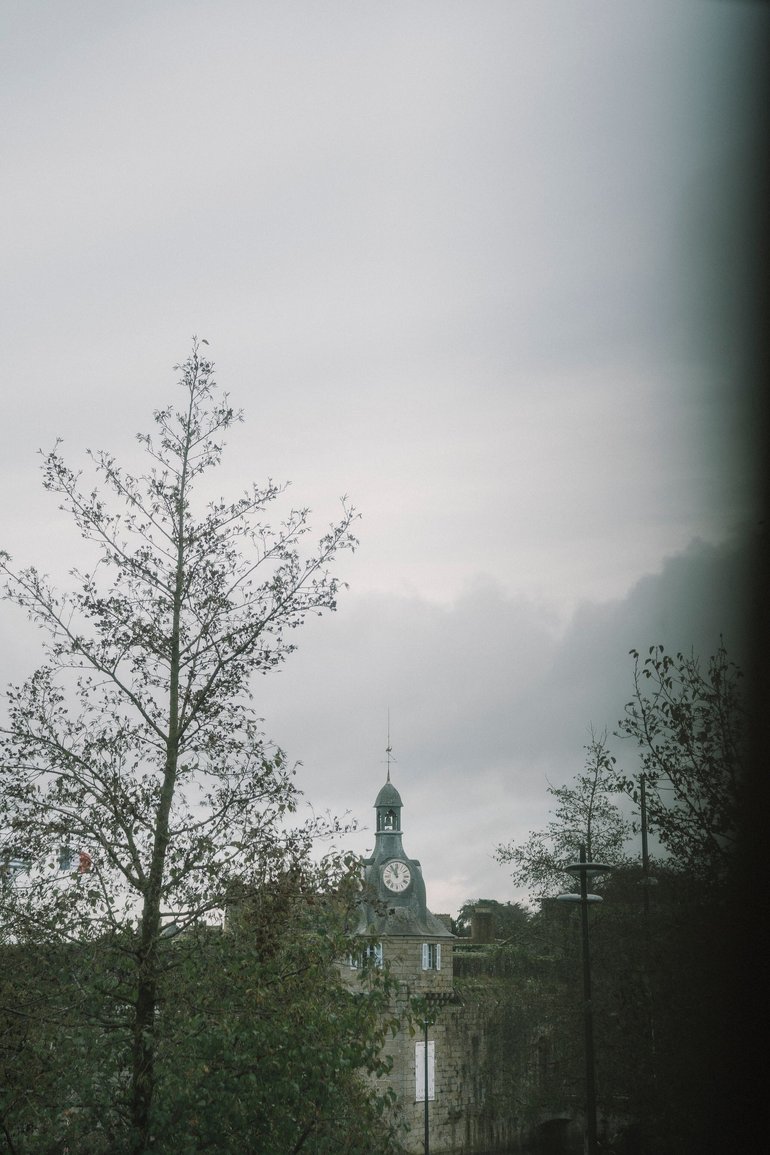 A building with a clock tower, surrounded by trees and a cloudy sky.