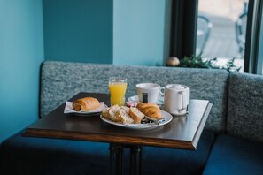 Ein Frühstückstisch mit Croissants, Orangensaft und Kaffee am Fenster.