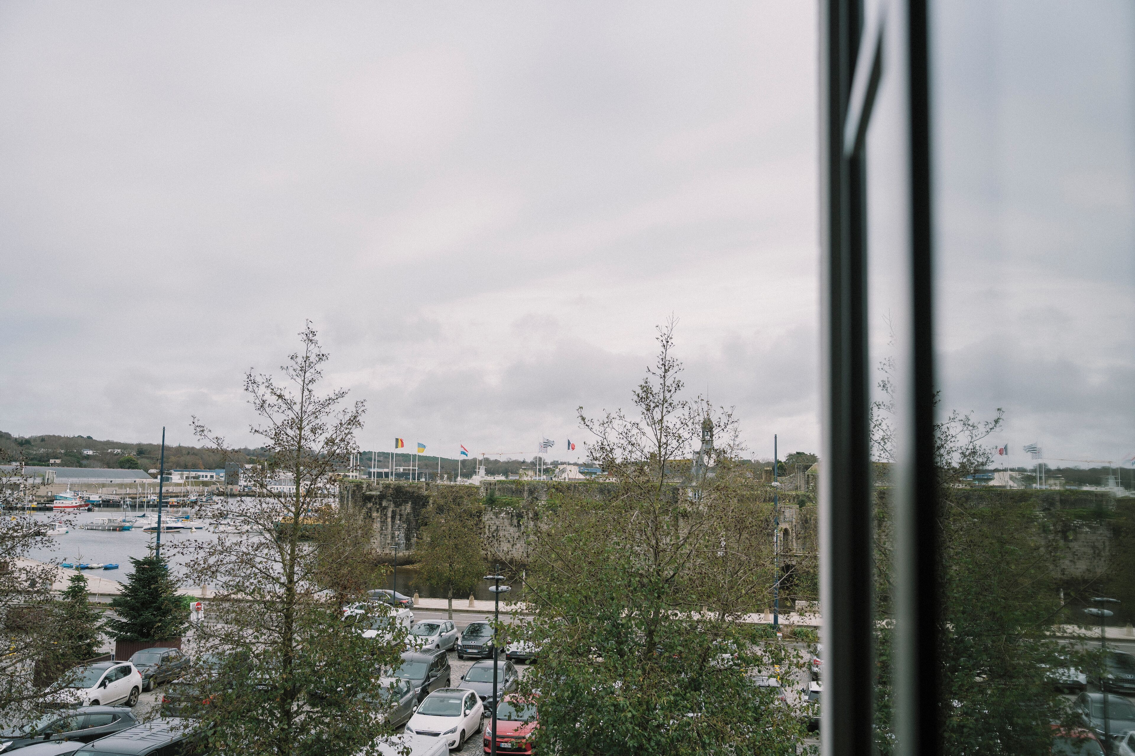 A parking lot with several cars, a building with a flag, and a cloudy sky.