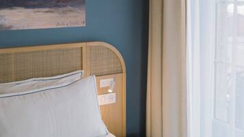 Ein Schlafzimmer mit einem Bett, einer Wandleuchte, einem Gemälde und einem Fenster mit Vorhängen.