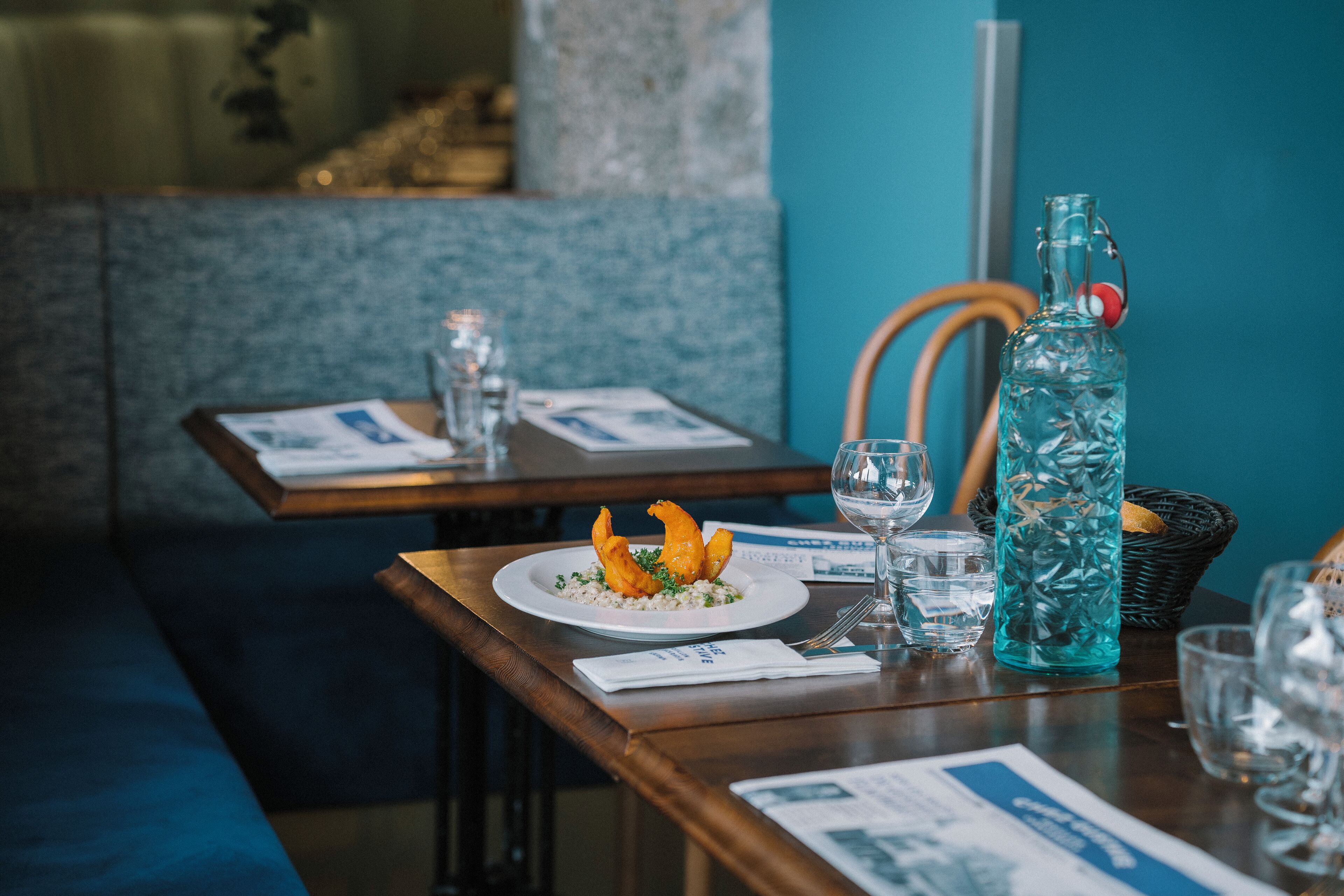 A restaurant setting with a table set for two, including plates of food, glasses, and a water bottle.