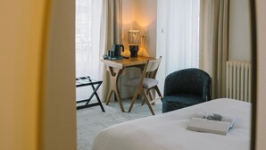 Una camera d'hotel con un letto, una scrivania con una sedia, una lampada e vista attraverso una finestra con tende.