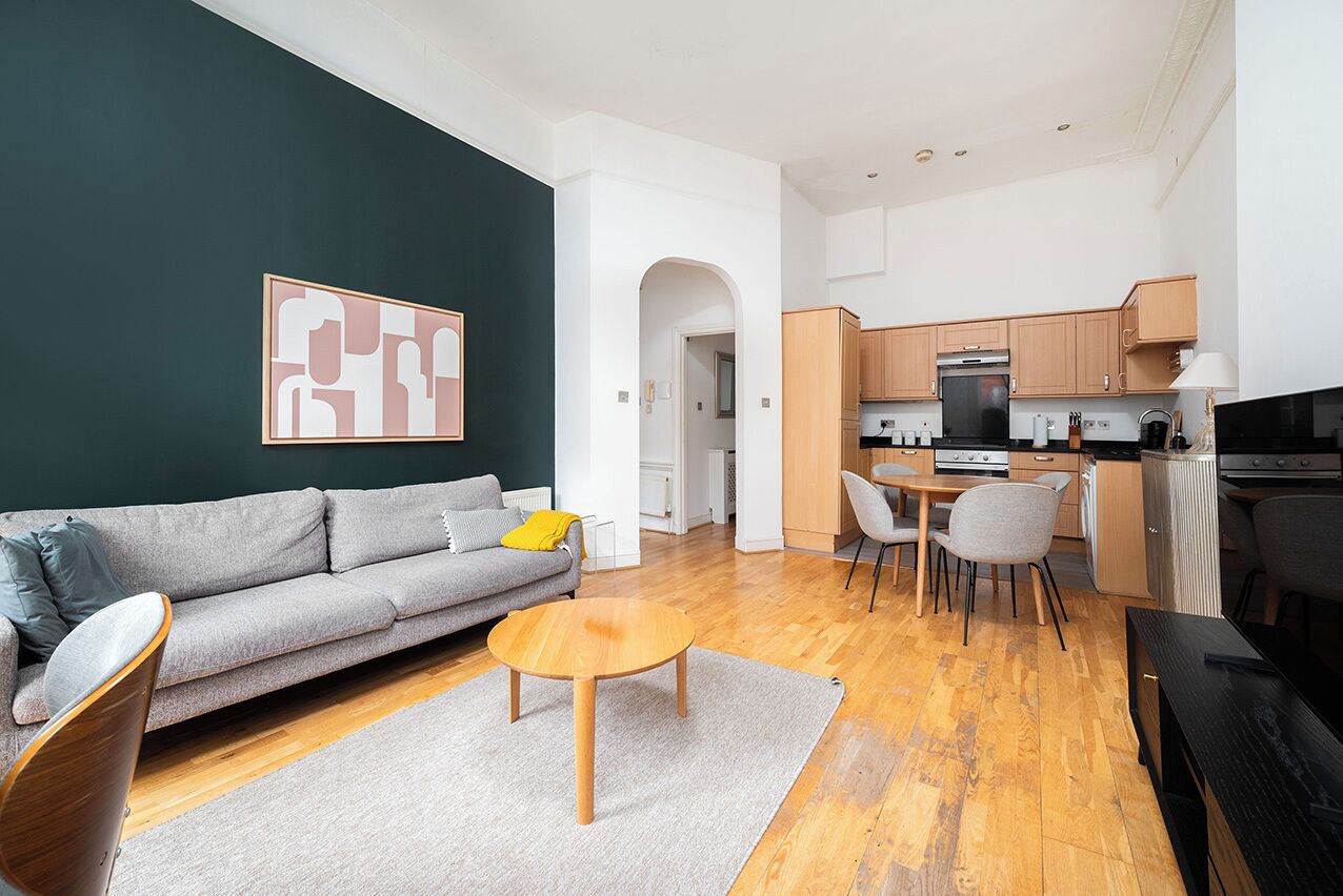 A modern living room with a grey sofa, a round wooden coffee table, and a dining area with a small table and chairs.