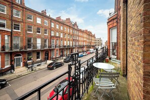 A street view with terraced houses, a red car, and a table with chairs on a balcony. - Marylebone Luxury 2-Bed Suite (London)