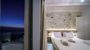 Une chambre d’hôtel avec un mur en pierre, un lit avec du linge de maison blanc, une table de chevet et une vue sur la mer.