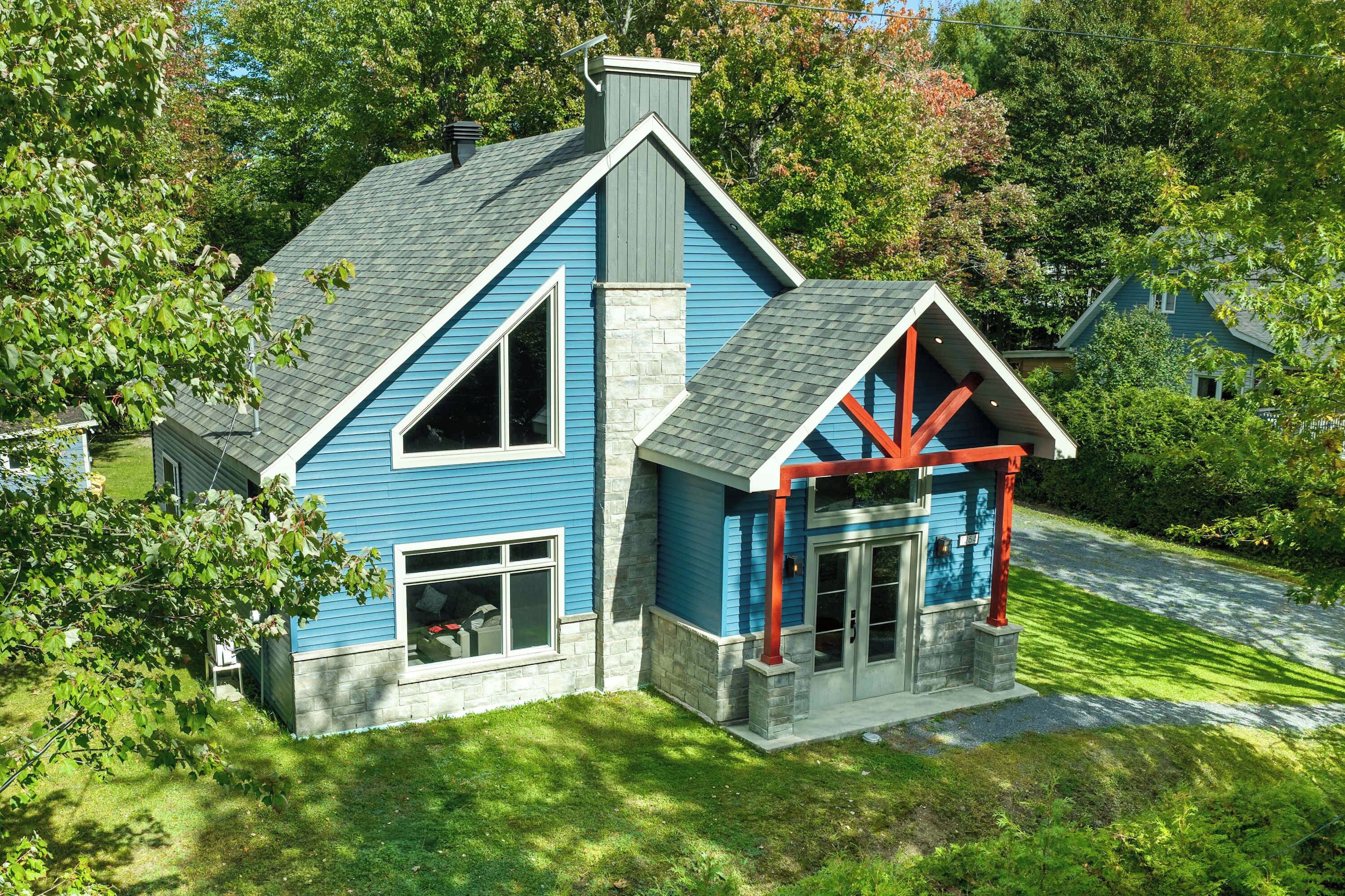 Une maison à deux étages, avec une façade bleue, une cheminée en pierre et un porche rouge.