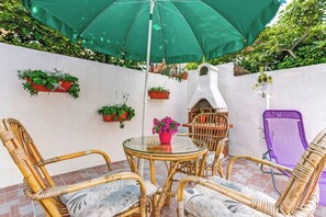 Eine Terrasse mit Korbmöbeln, einem Glastisch und einem grünen Sonnenschirm.