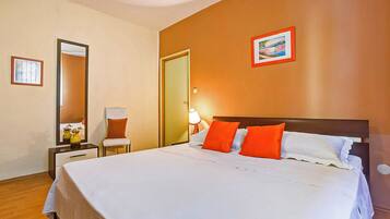 A hotel room with a large bed, a nightstand with a lamp, a chair, and a mirror.