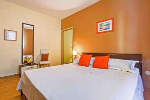 Ein Hotelzimmer mit einem großen Bett, einem Nachttisch mit Lampe, einem Sessel und einem Spiegel.