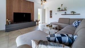 Uma sala de estar moderna com televisão de tela plana, sofá, mesa de centro e prateleiras decorativas.