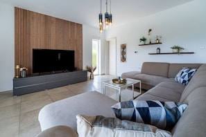 Ein modernes Wohnzimmer mit Flachbildfernseher, einer Couch, einem Couchtisch und dekorativen Regalen.