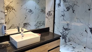 Ein modernes Badezimmer mit Waschtisch aus Marmor, einem großen Spiegel und einer Duschkabine aus Glas.